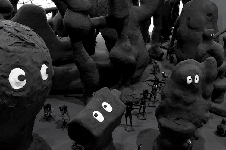 A largescale sculptural installation of cartoon-like shadow figures. These anthropomorphic sculptures are modelled from painted black modelling clay, foam, and resin, and evocative of the French animation Barbapapa.