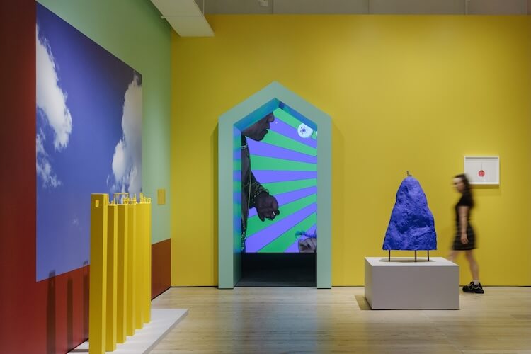 Yellow walled gallery space with bright installations