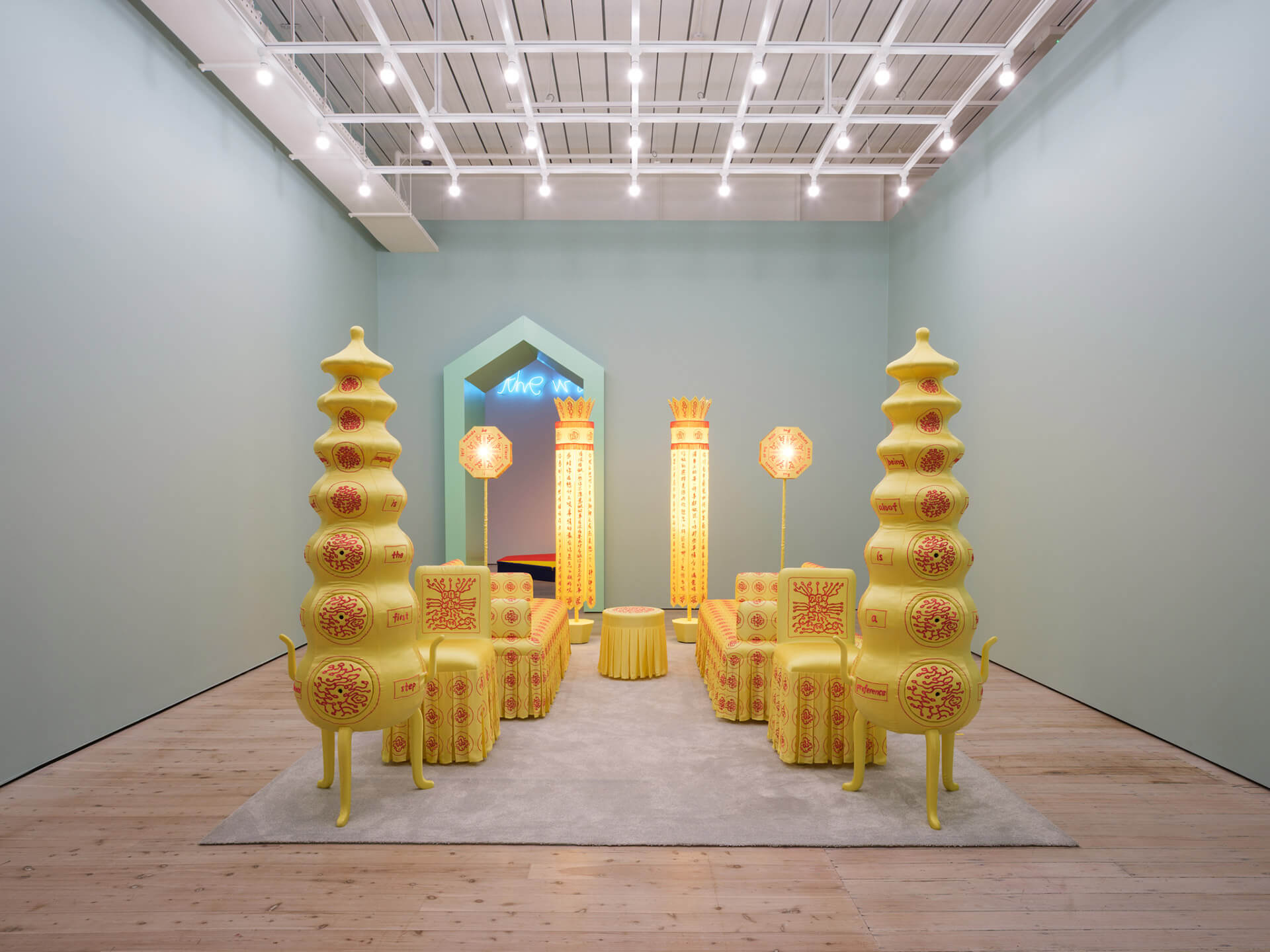 Complete gallery view of yellow installation with Chinese calligraphy, decorated furniture, and geometric ceiling structure