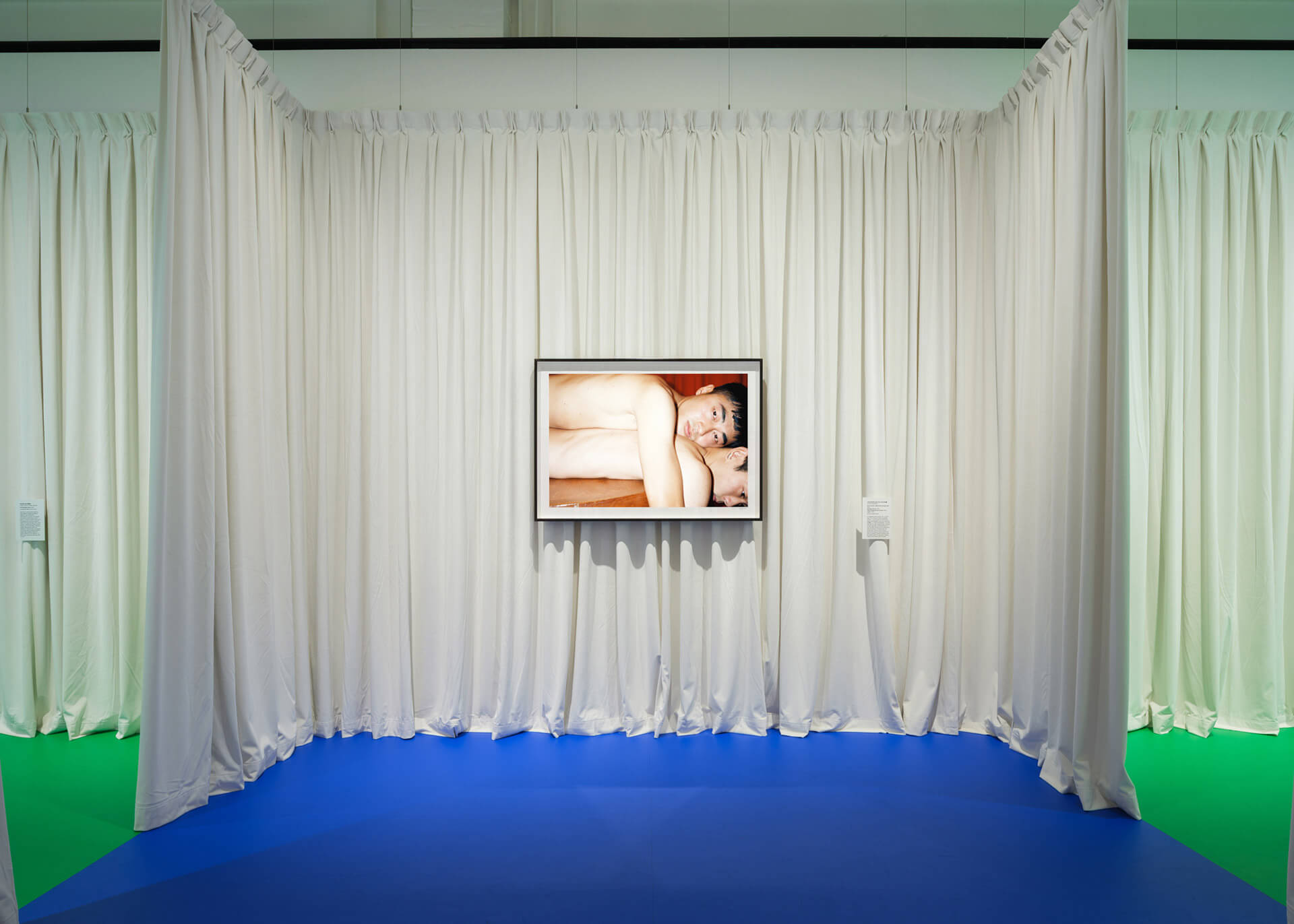 Detail of photography installation by Lin Zhipeng showing curtained space with blue floor and intimate portrait display