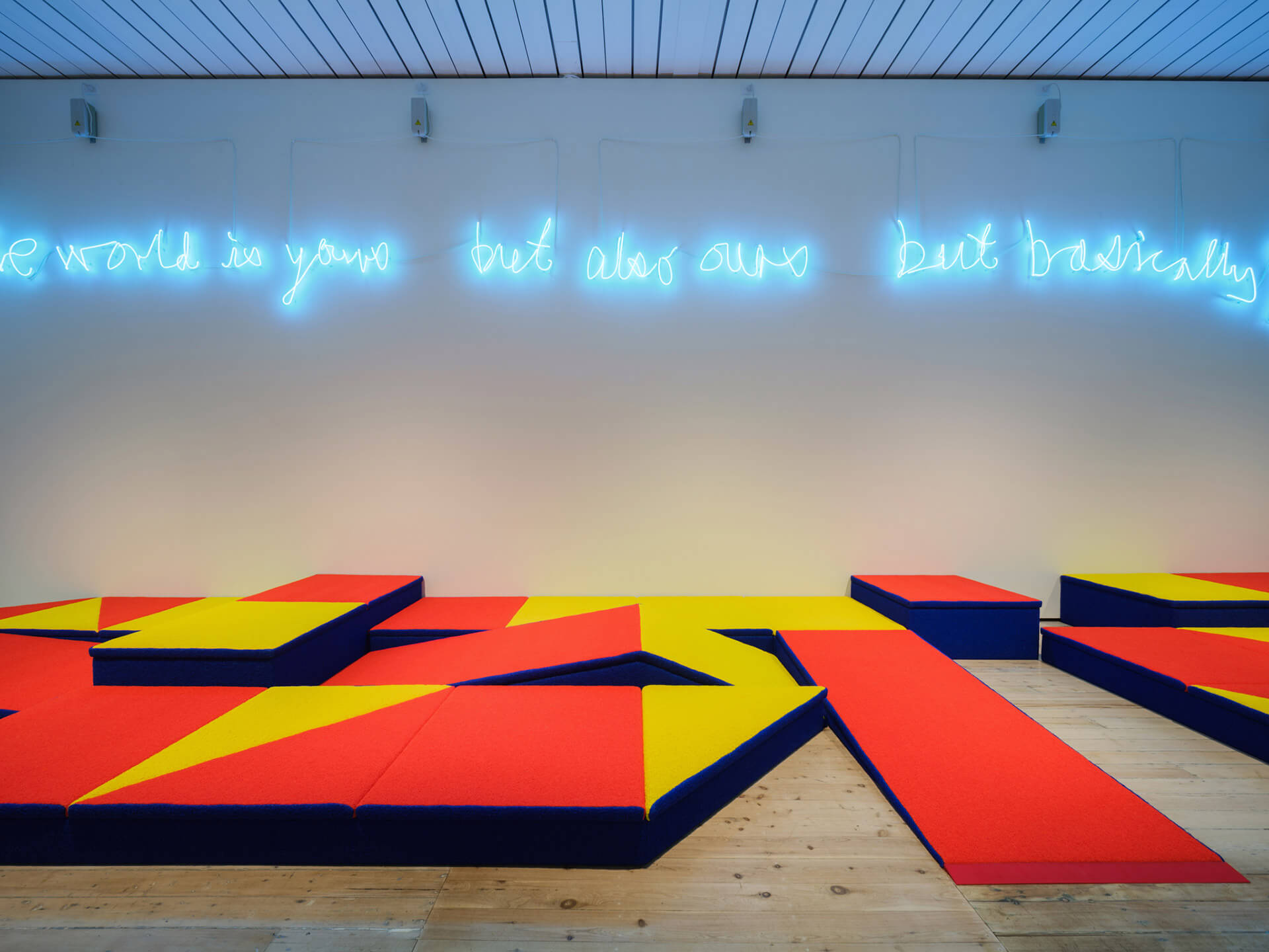 Complete installation Risers by Samson Young with blue neon text above geometric red and yellow seating elements