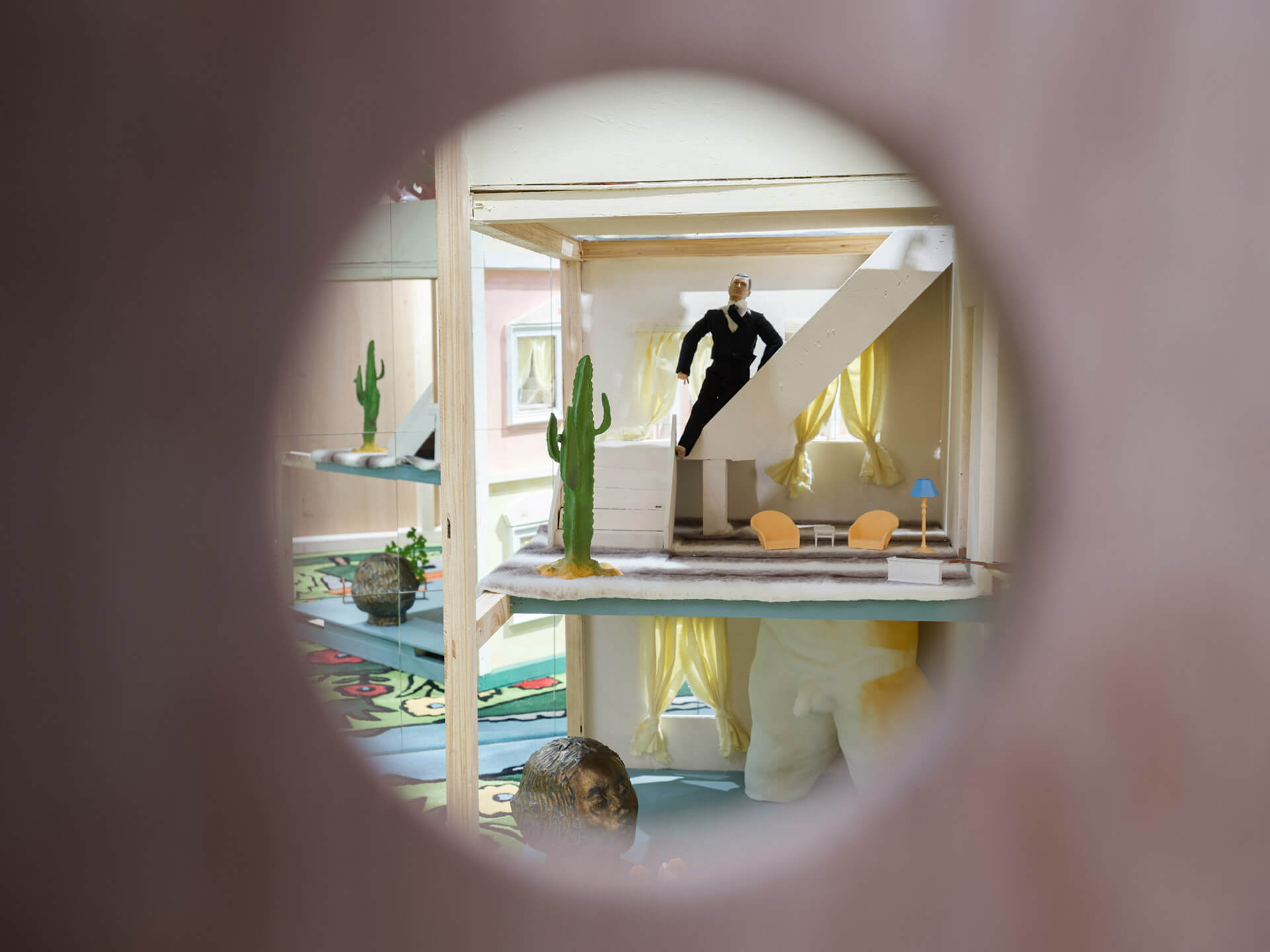 Circular window view into Shih-Yung-Chun's "Private Hotel 8" installation with figure, cactus plants, and colorful furnishings at White Rabbit Gallery