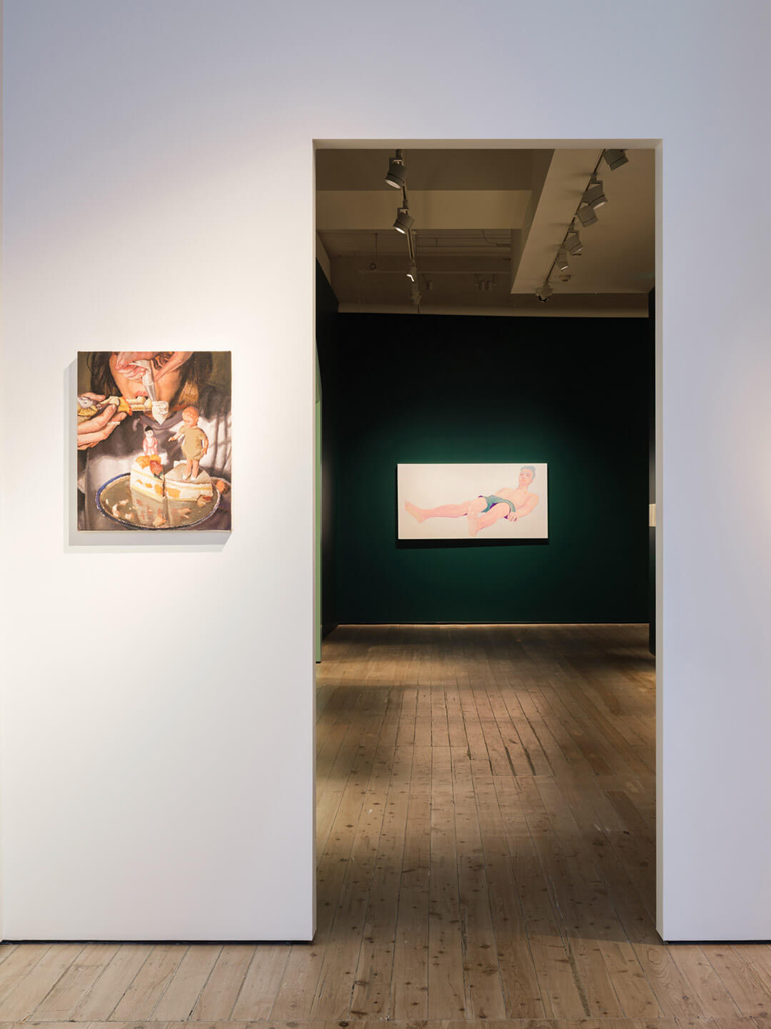 Gallery corridor view showing contemporary paintings on white and dark green walls with wooden flooring