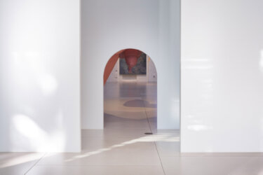 Minimalist white gallery corridor with arched doorway leading to adjacent exhibition spaces