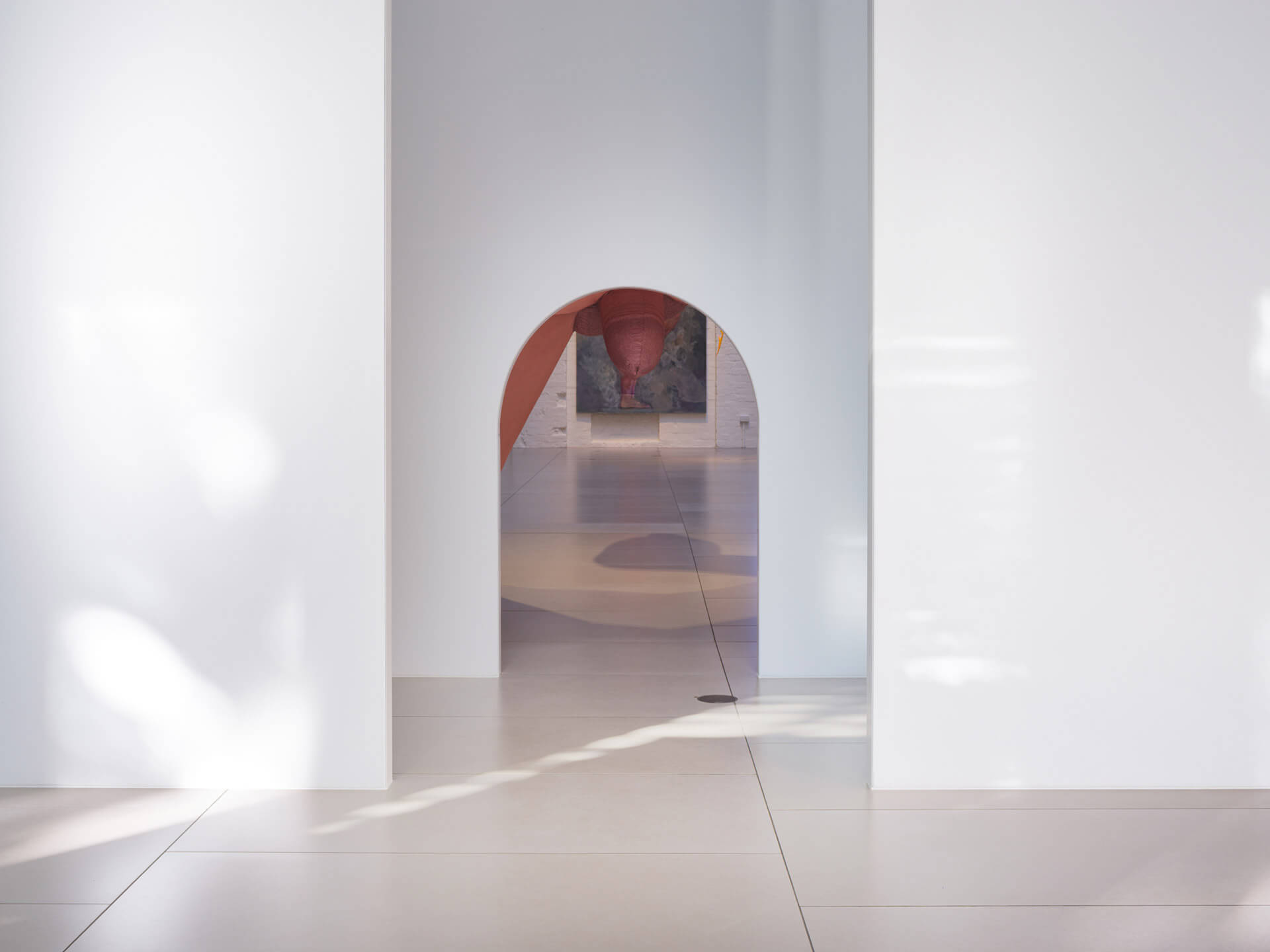 Minimalist white gallery corridor with arched doorway leading to adjacent exhibition spaces