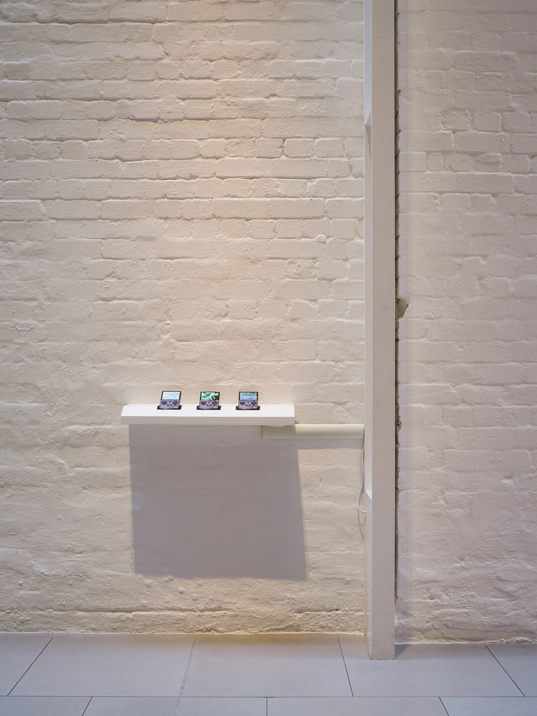Gallery installation showing small digital screens by Xia Han from "Humiliation 2" series displayed on white pedestal against brick walls