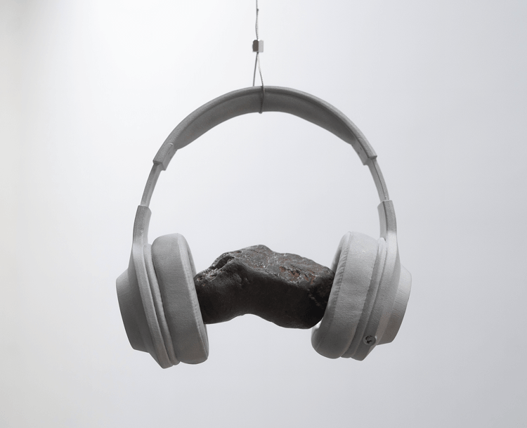 An hanging installation of headphones made out of aluminum with a meteorite rock between the ear pieces.