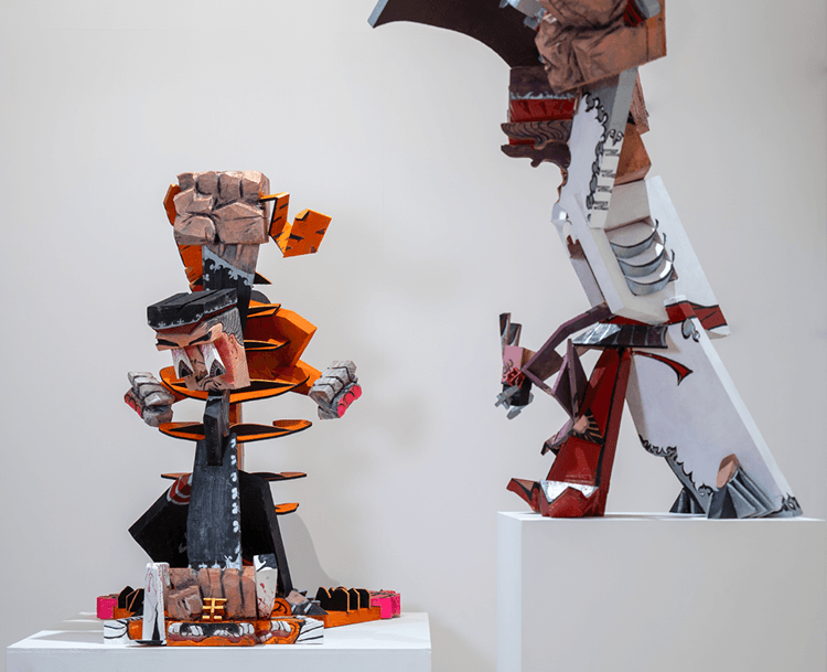Two sculptural figures made from wood, and painted in red, orange, blue and white.