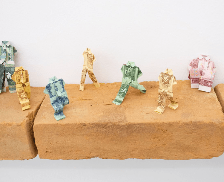 Bank notes folded into the shape of walking figures, on a brick shelf.