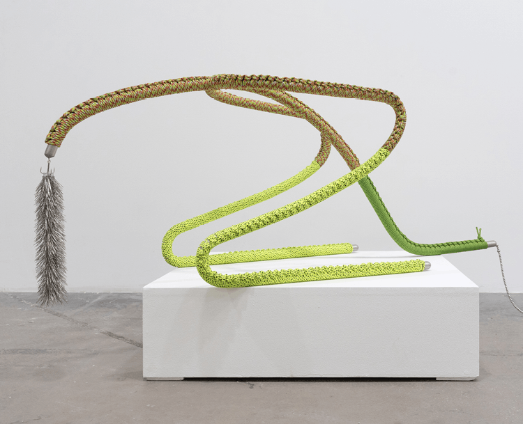 An installation on a white plinth. A sclupture made from rope, metal and a fish hook.